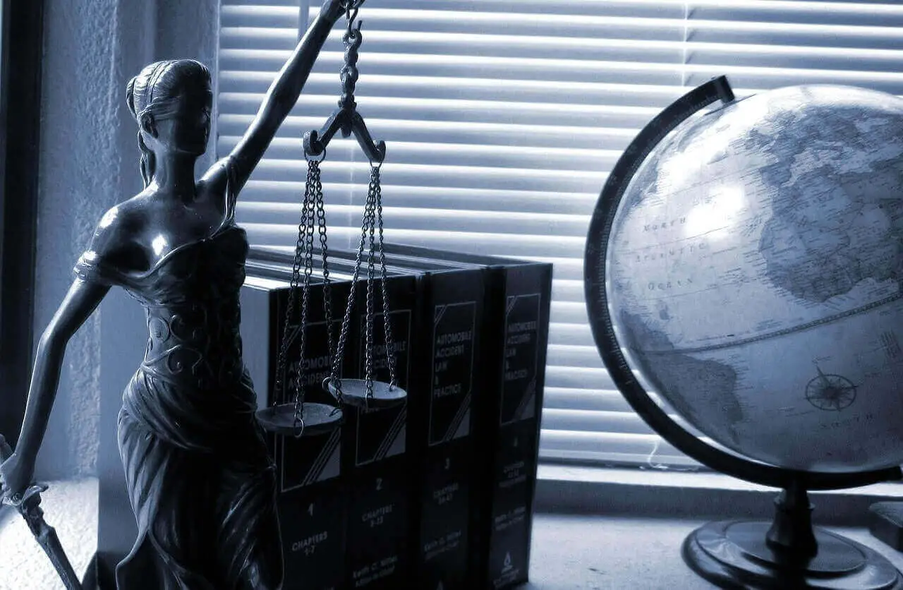 justice statue holding scales in front of books and globe on desk