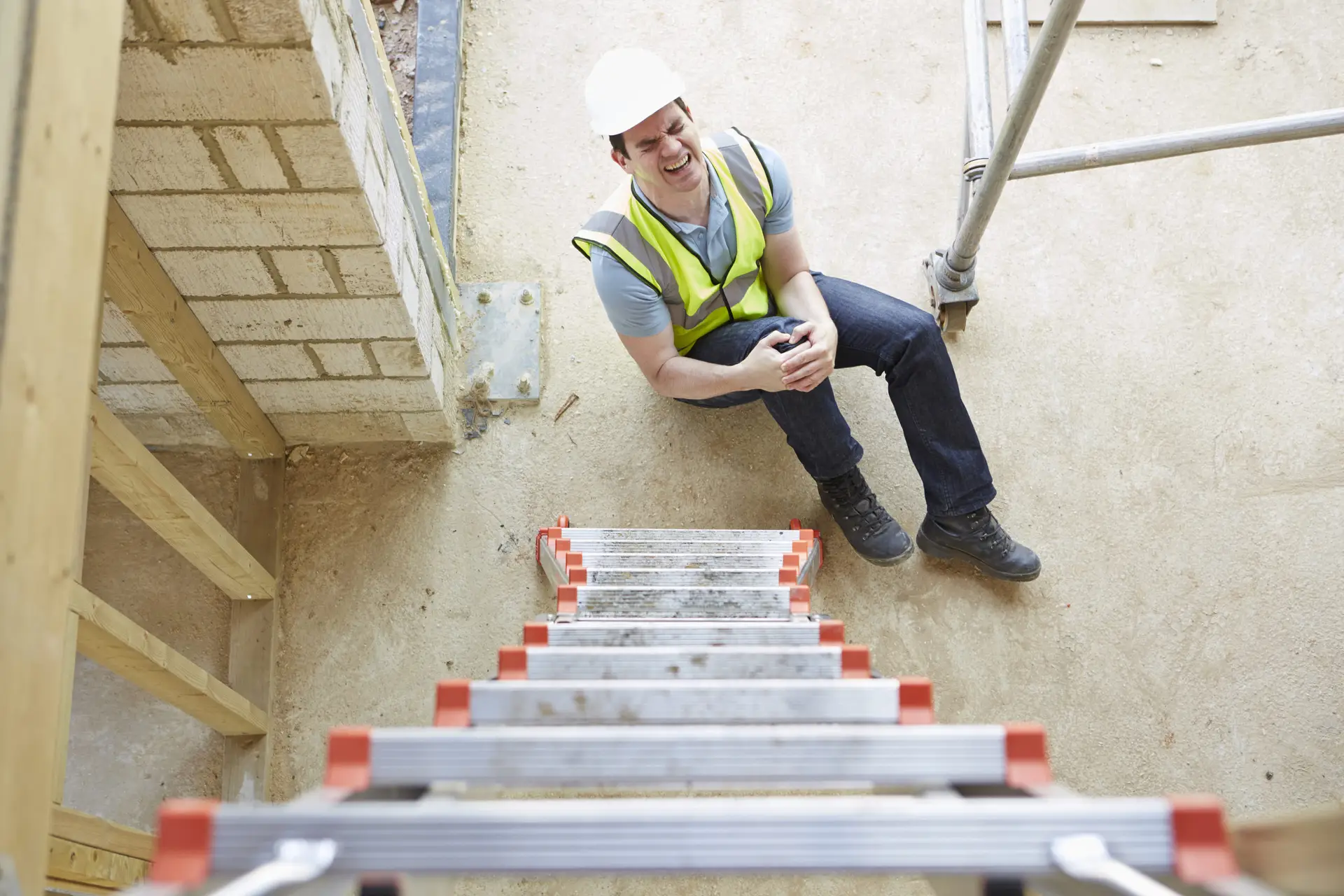 construction worker sitting on floor gripping knee and wincing
