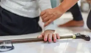 A senior’s hand holding a cane on the floor after a slip and fall, with assistance being offered.