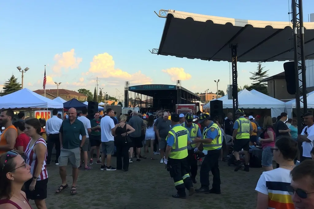 A summer festival during the day, with a lively crowd, food stands, and a music stage.